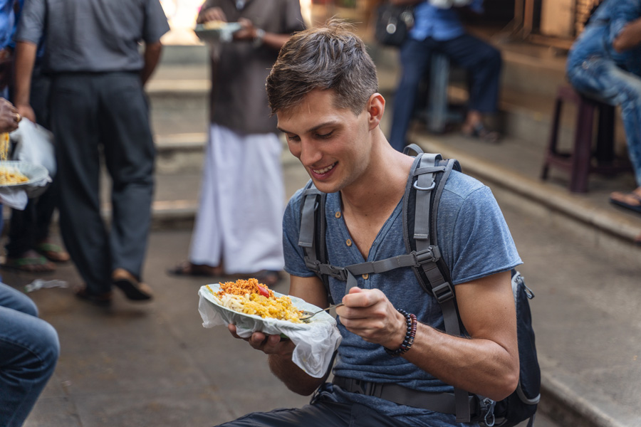 A boy sitting by a road enjoying a plate of street food in Sri Lanka, witnessing an experience that is never to be missed.