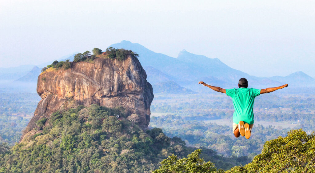 A boy in a green t-shirt jumped up on a rock top, with another rock in its background