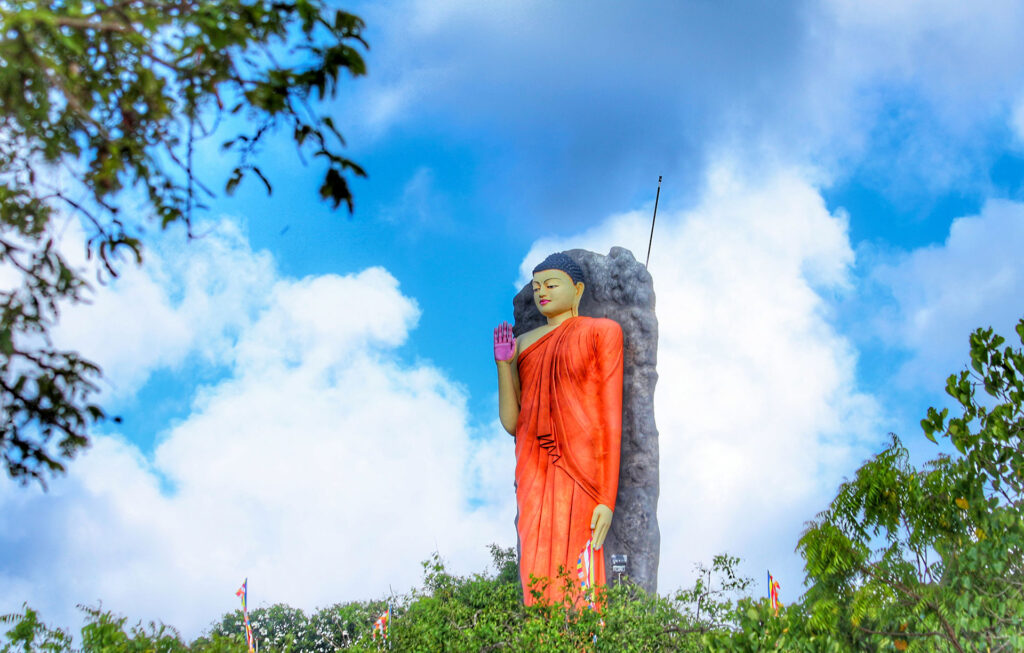 A buddha statue that stands high with the blue sky as the background