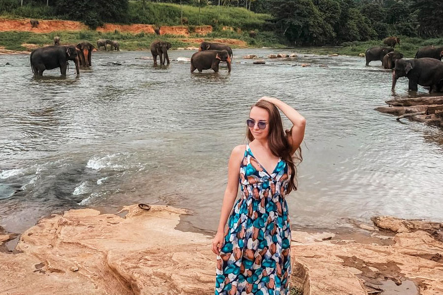 A girl wearing a blue frock on a rocky terrain in front of stream with few elephants