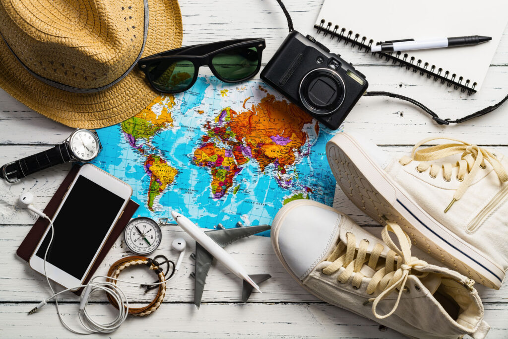 watch, shoes, camera, phone, hat, pen, and compass, featuring the best travel essentials to pack when travelling.