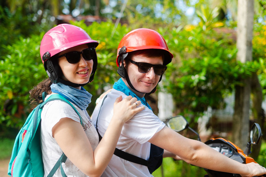 A foreign young couple riding a bike wearing helmets, as it is one of the things that you should NOT avoid to make your stay amazing and hassle-free in Sri Lanka