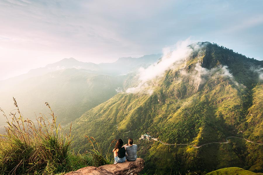 A foreign couple on a mountain top, seated and observing the surroundings, during a honeymoon in Sri Lanka!