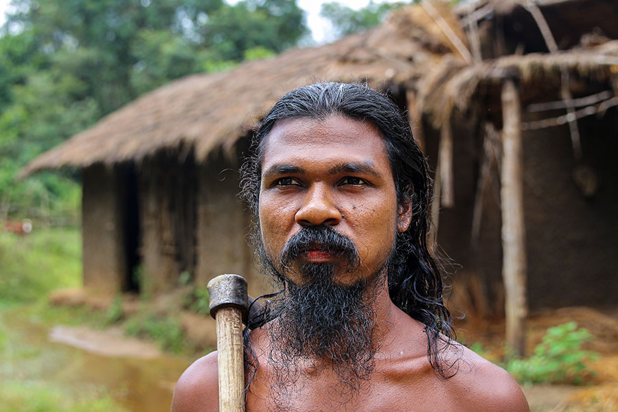 A Vedda Man with bare shoulders, standing in front of a forest, who belongs to the Indigenous Community of Sri Lanka